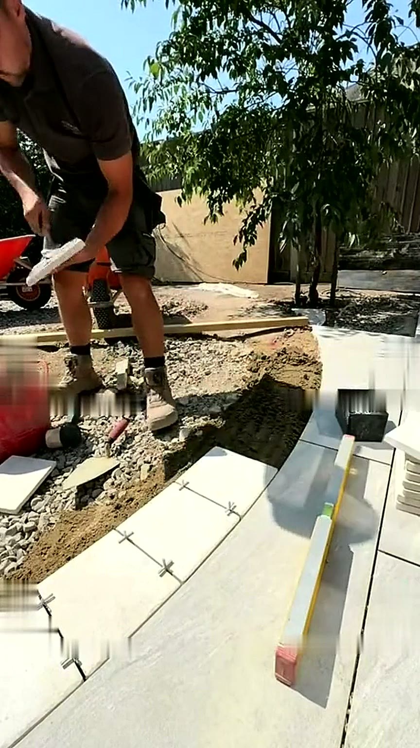 Curved pale kerb and porcelain slabs being laid to form the garden geometry