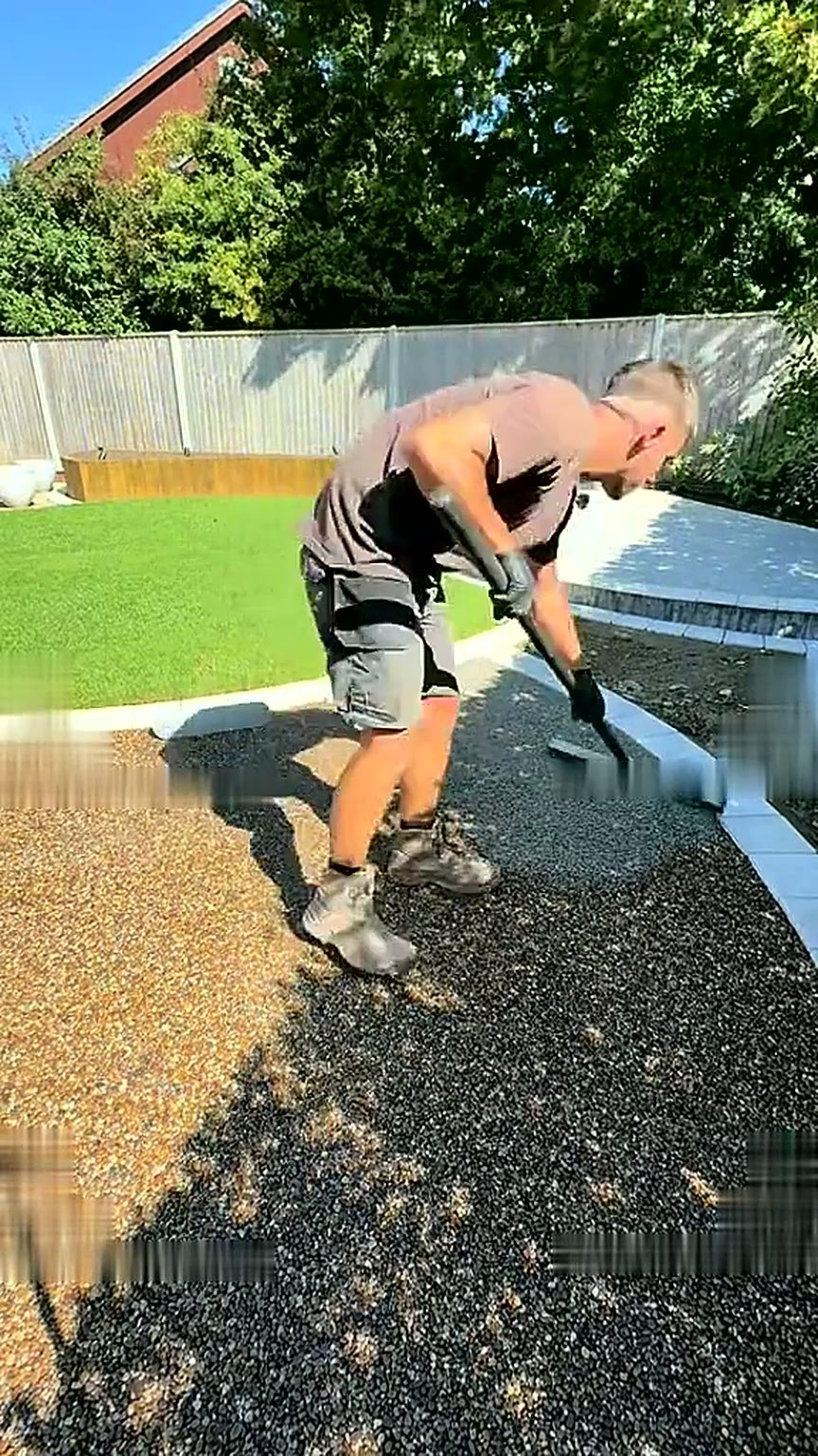 Installer spreading resin bound aggregate across a permeable base with a rake