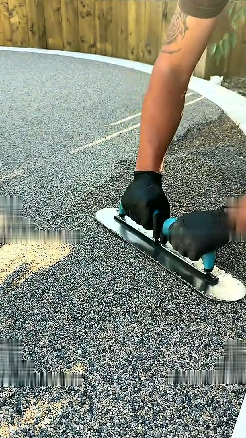 Installer hand-trowelling the resin surface smooth beside a pale kerb