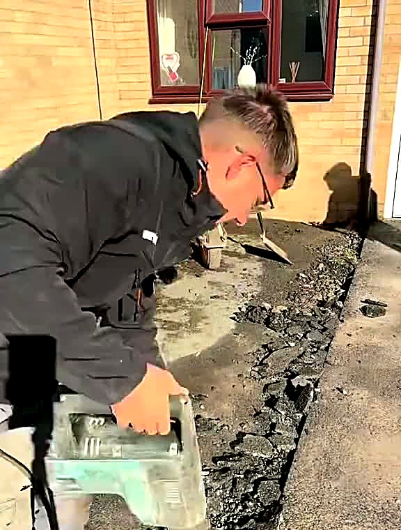 Installer breaking out old concrete beside a house wall with a breaker