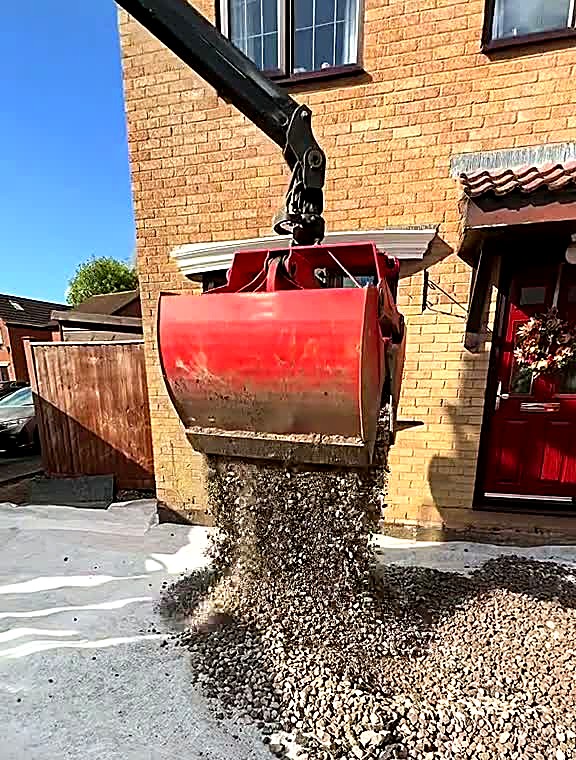 Grab bucket tipping sub-base stone onto a prepared driveway formation