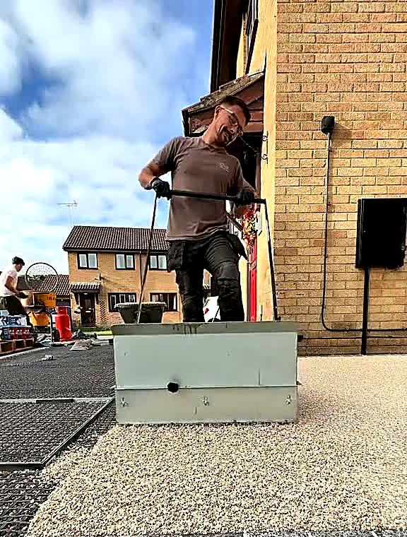 Pale gold resin bound aggregate being spread across a prepared driveway