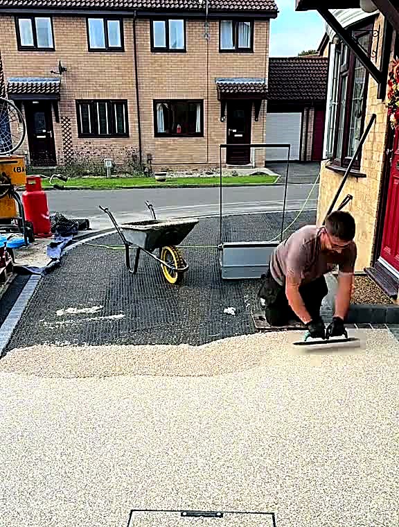 Installer hand-trowelling resin bound surface smooth across a driveway