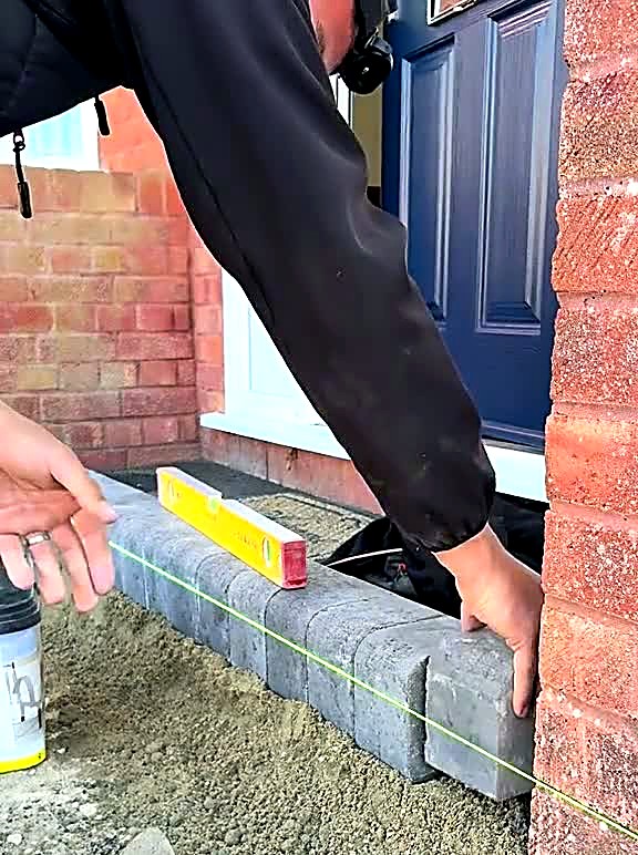 Installer levelling a kerb block beside a front door with a spirit level