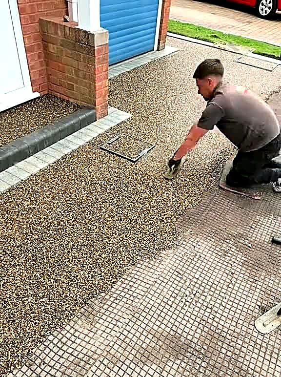 Installer spreading resin bound gravel across a prepared driveway base