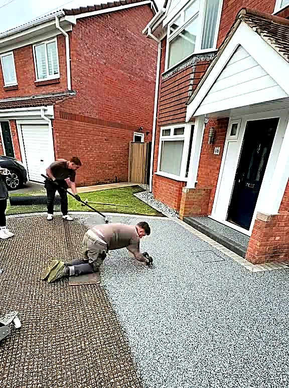 Silver-grey resin driveway being finished in front of a brick house