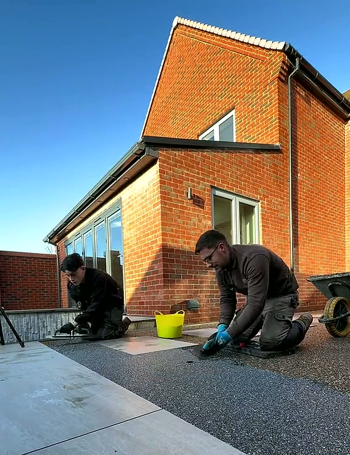 Two installers kneeling to trowel a resin surface beside a modern house